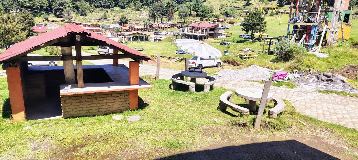Palapa con asador de ladrillo y mesas de piedra frente a las instalaciones