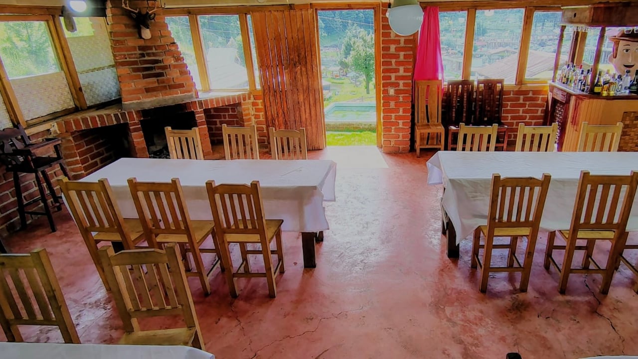 Salón techado con mesas largas vestidas de mantel blanco y sillas de madera