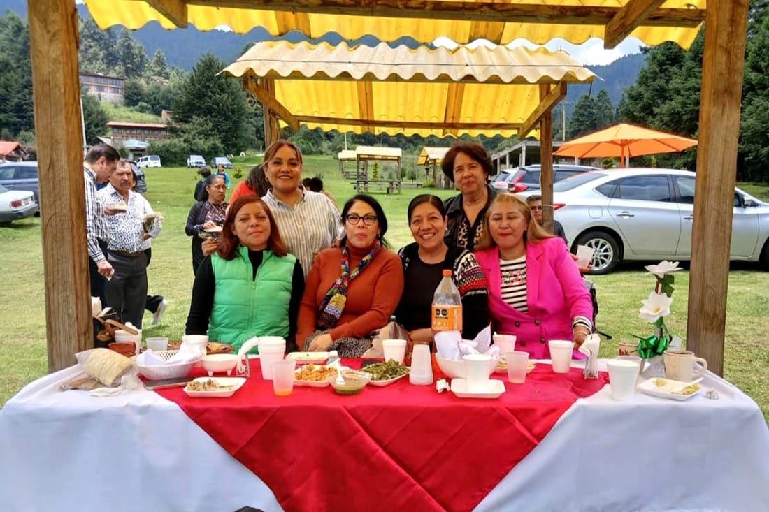 Grupo de invitadas compartiendo platillos en mesa larga con mantel rojo