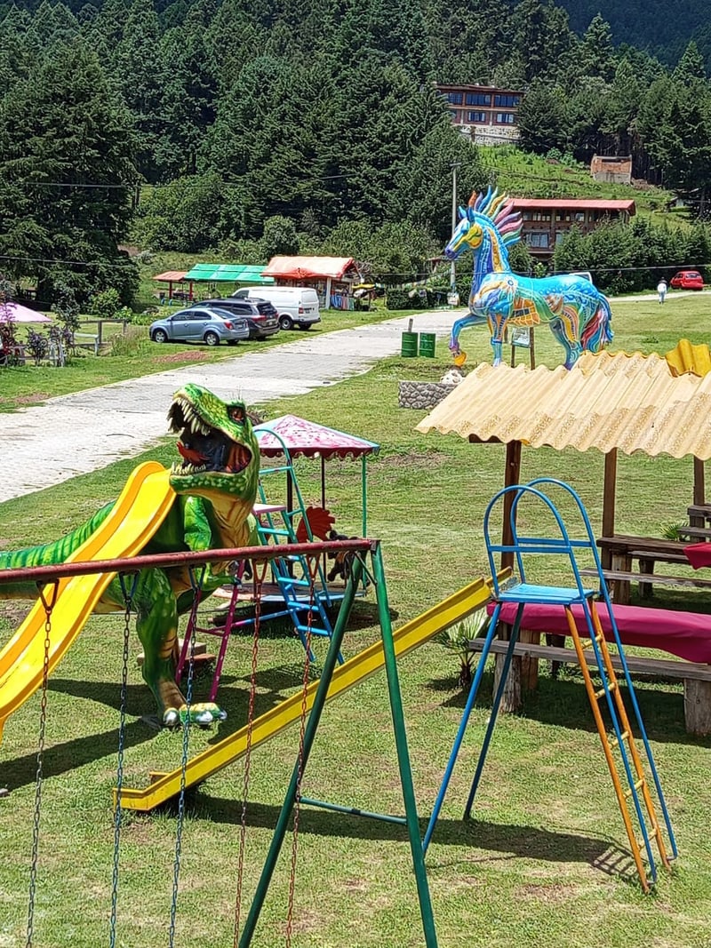 Resbaladilla con figura de dinosaurio verde junto al caballo alebrije